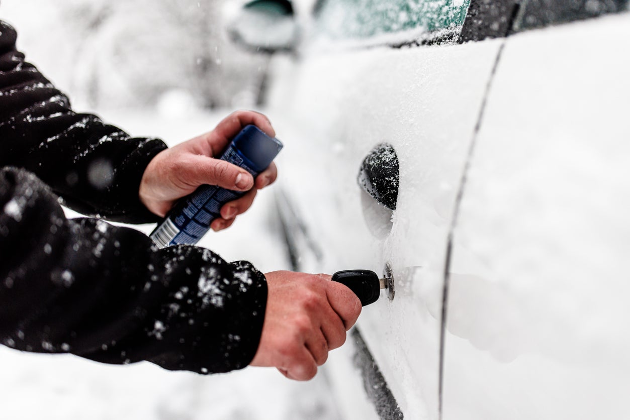 A Man has Snow Problems with a Car so he is Unfreezing the Door.