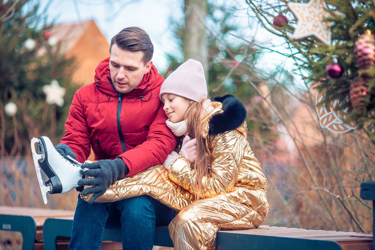 Family winter sport. Father helps a kid put on skates