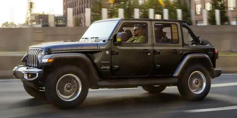A brand new black 2023 Jeep Wrangler driving down city streets.