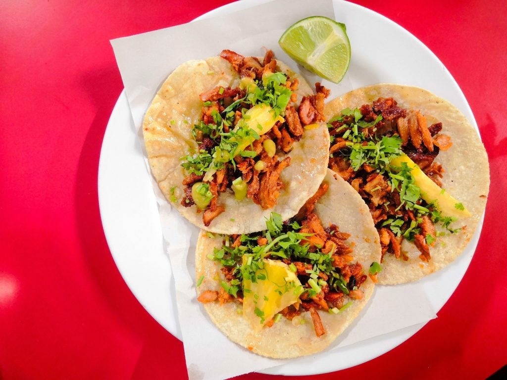 Areil shot of seemingly pulled pork street tacos with pineapple and a variety of vibrant greens