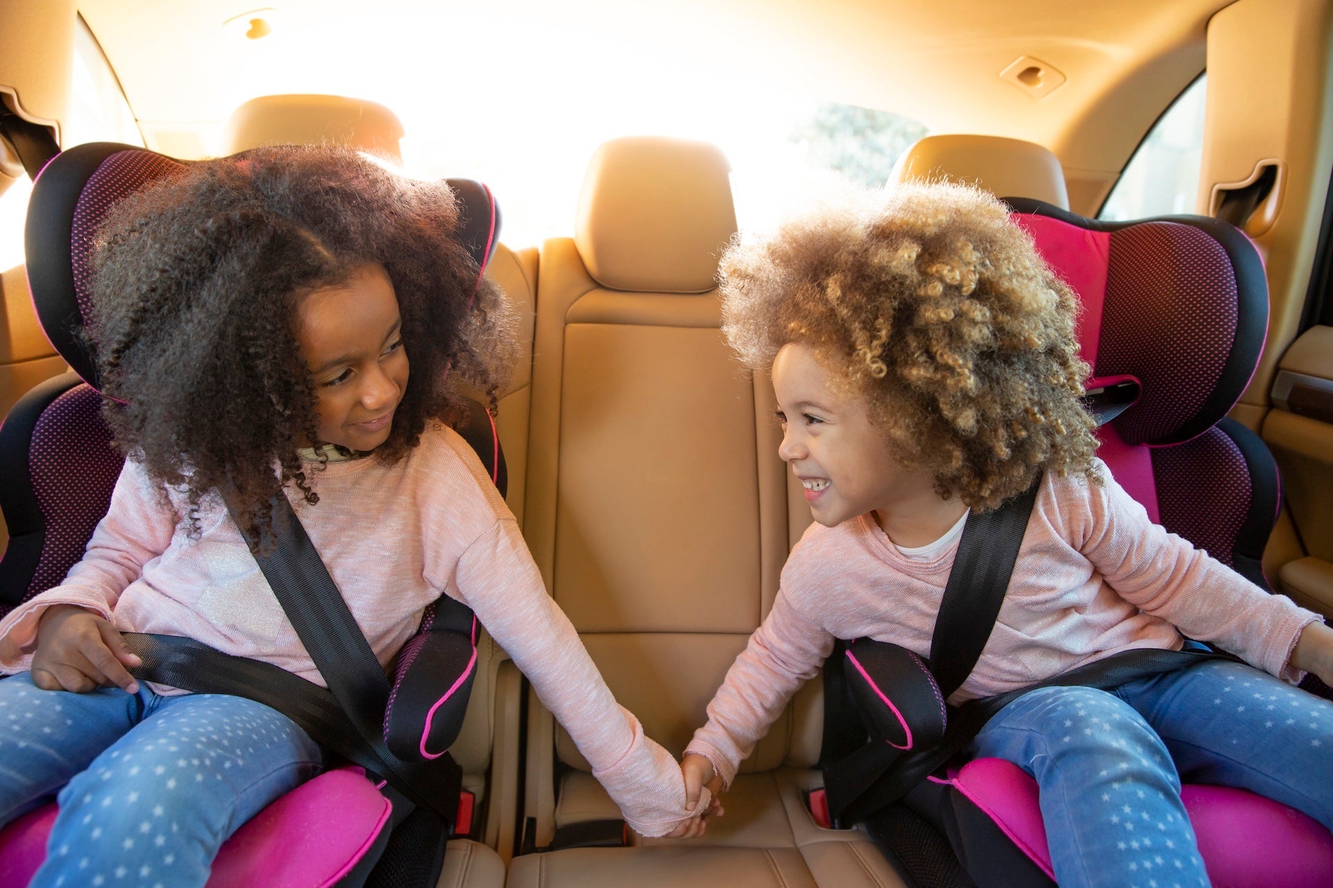 Kid sister girls in car back seat with safety belts holding hands smiling