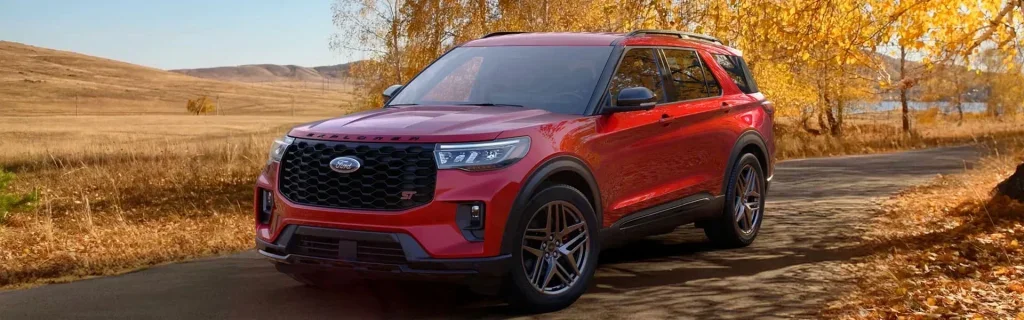 Red Ford Explorer SUV parked on a scenic fall road.
