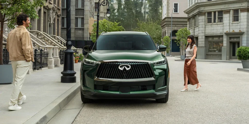 2026 INFINITI QX60 in green parked on a city street with a man and woman standing nearby.