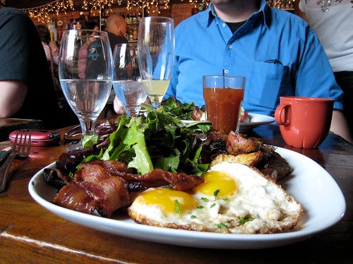 Plate with over-easy eggs, bacon, potatoes, and greens at brunch restaurant