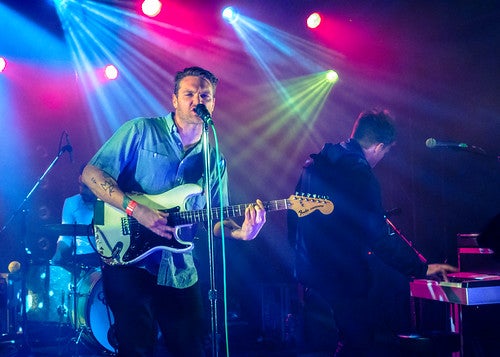 A musician singing and playing guitar on stage under concert lights