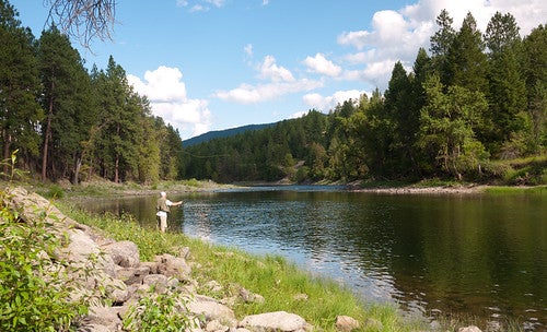 Man casting fishing line into Red River from river bank