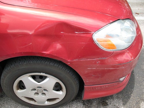 Red car with a dent in it above front right tire well, in need of paintless dent repair