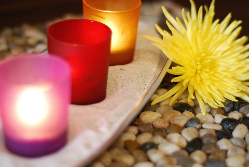 Tea light candles in colored glasses on a ledge next to decorative stones