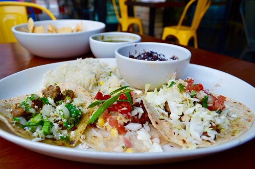 Three handcrafted tacos on plate with black beans and rice