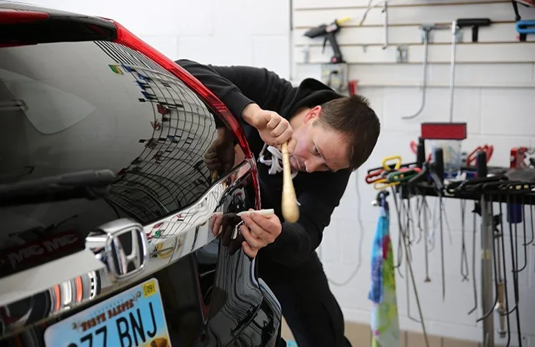 Auto Technician fixing a dent using paintless dent repair techniques
