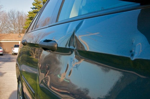 Close up picture of a dent by the handle of a black sedan