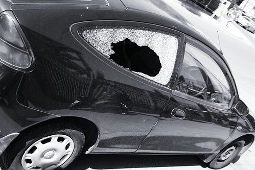 Black and white photo of a car with the back passenger side window broken