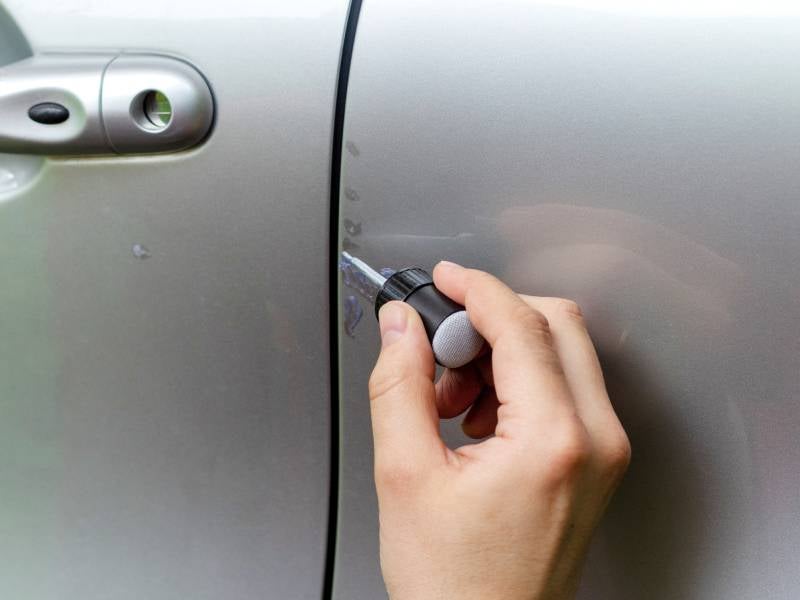 person applying scratch repair kit to a car