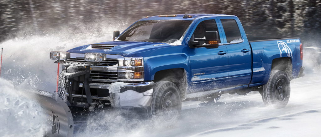 A blue Chevy Silverado 1500 Alaskan plowing through snow outside