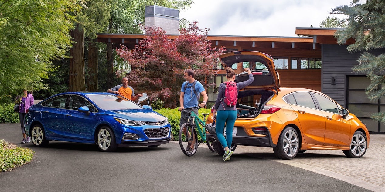 A couple entering a blue 2017 Chevy Cruze Sedan with a couple placing their bikes into an orange 2017 Chevy Cruze Hatchback.