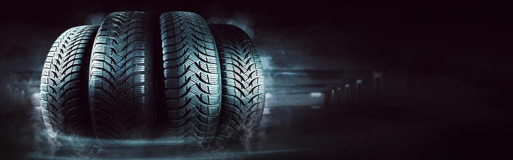 Four new car tires with dramatic lighting and mist.