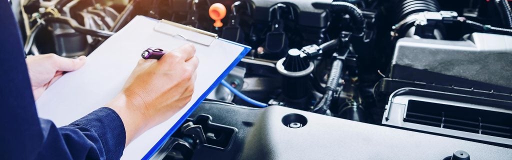 Mechanic inspecting a car engine with a clipboard.