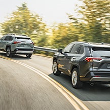 Model Features of the 2021 Toyota RAV4 at Bennett Toyota | Two RAV4s driving fast around a turn showing back of car