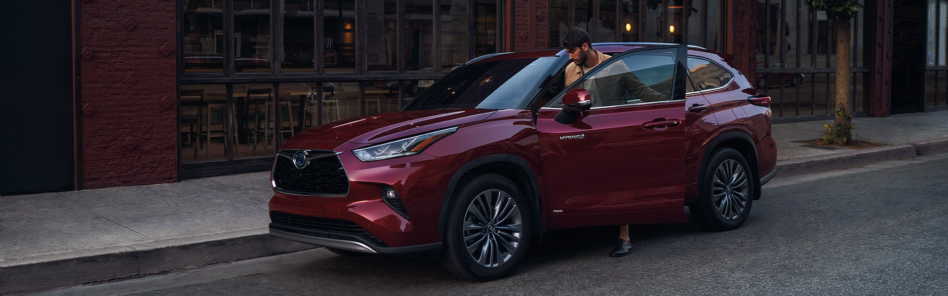 Model Features of the 2022 Toyota Highlander Hybrid at Bennett Toyota | Man Getting Into Driver's Side of Red Highlander Hybrid Street Parked in City