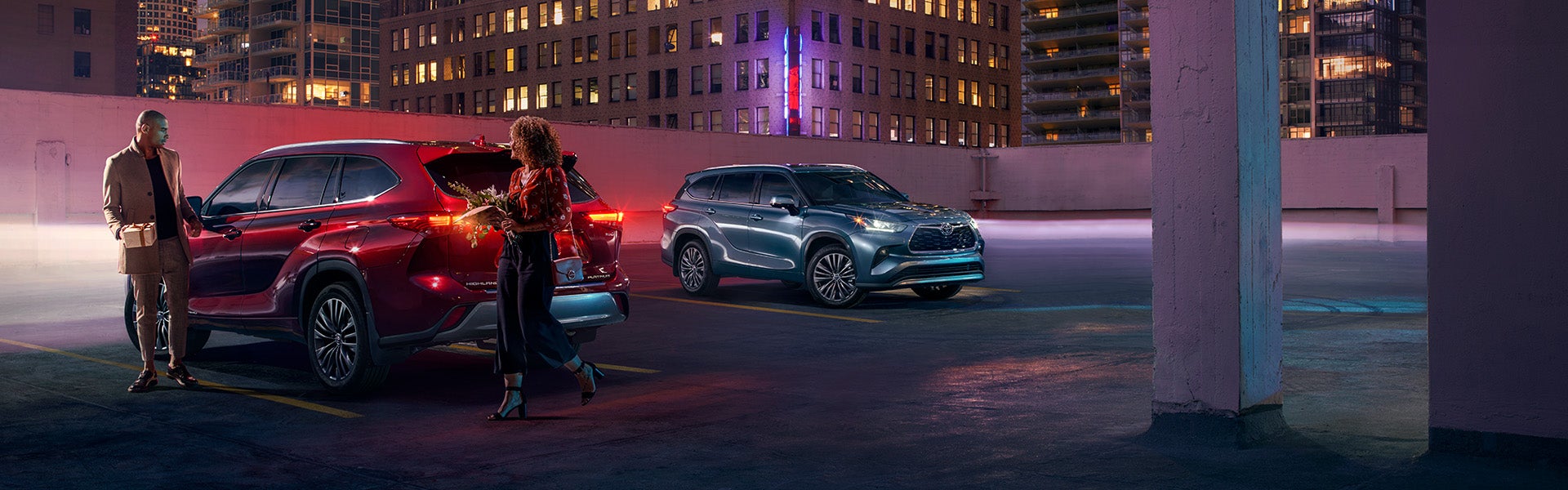 Model Features of the 2022 Toyota Highlander Hybrid at Bennett Toyota | Blue and Red Highlander Hybrid Vehicles Parked Next to Each Other on Top Floor of City Parking Garage at Night