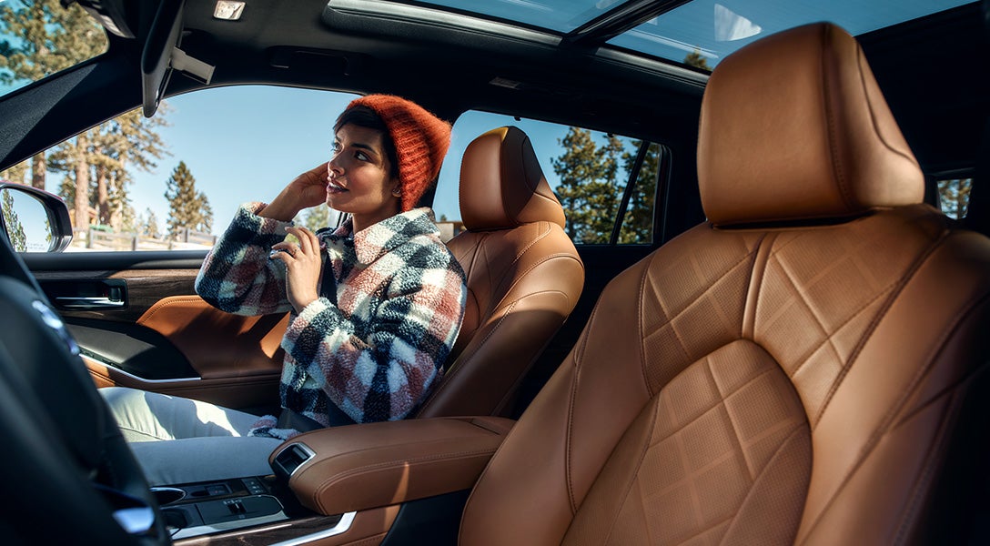 Model Features of the 2022 Toyota Highlander Hybrid at Bennett Toyota | Passenger Using Mirror While Sitting Inside Highlander Hybrid - Featuring Tan Leather Interior