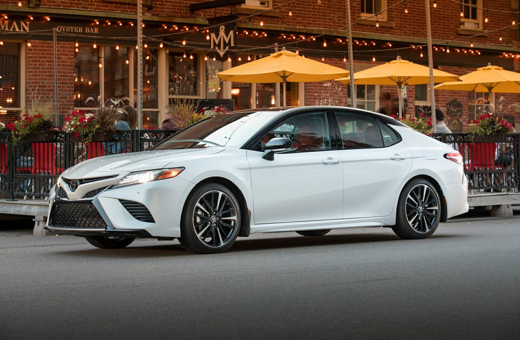 Image of a white 2019 toyota camry parked outside a restaurant in the evening.