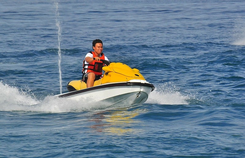 A man riding a yellow jet ski out in open water wearing an orange vest